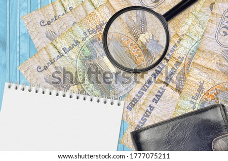 25 Egyptian piastres bills and magnifying glass with black purse and notepad. Concept of counterfeit money. Search for differences in details on money bills to detect fake