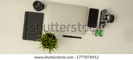 Top view of worktable with laptop, smartphone, camera, stationery and decoration on white table 
