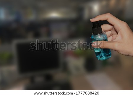 A bottle of alcohol sprayed in the hand against the blurred office background.Preparing to prevent office space infection in the corona virus outbreak.