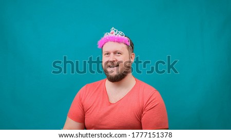 Cute bearded freaky man in a pink T-shirt with a deadema on his head dreams with a magic wand in his hand. A funny wizard joke to make and fulfill a wish