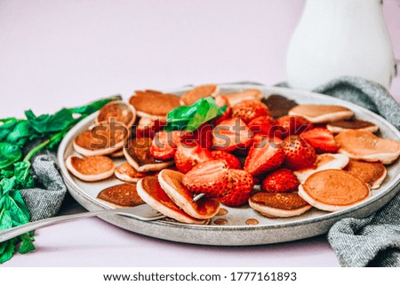 Plate with Traditional Pancakes and Tiny Pancake Cereal with Strawberries and Mint Leaves on a Dark Background. Trendy food. Mini cereal pancakes