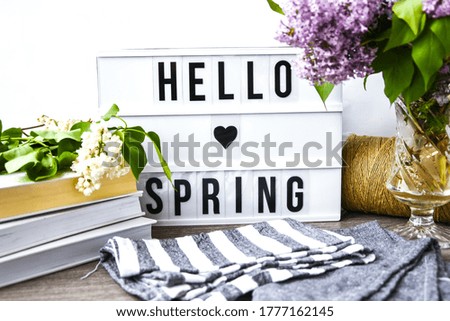 Lightbox with text GOOD MORNING and bouquet of violet lilac flowers in glass vase, spring time, books and rope, holiday background