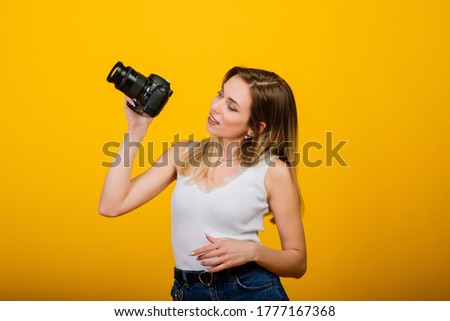 Excited female photographer working in studio. Portrait of stunning blonde girl with camera.