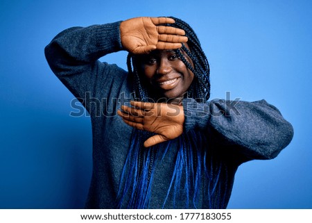 African american plus size woman with braids wearing casual sweater over blue background Smiling cheerful playing peek a boo with hands showing face. Surprised and exited