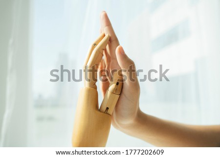 Hand of wooden cyborg robot and human touching each other.