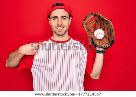 Young handsome sporty man with blue eyes playing baseball using glove and ball with surprise face pointing finger to himself