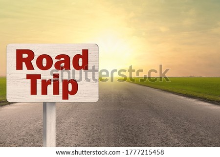 Wooden plaque with inscription road trip on asphalt highway at sunset