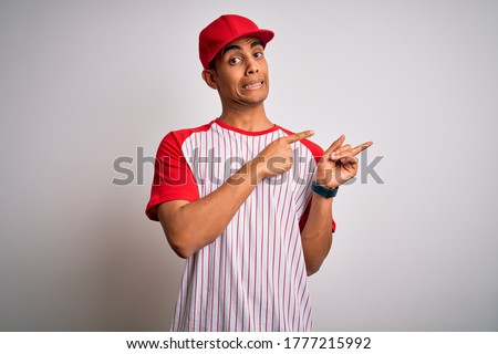 Young handsome african american sportsman wearing striped baseball t-shirt and cap Pointing aside worried and nervous with both hands, concerned and surprised expression