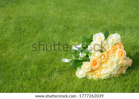A large bouquet of white and beige roses lies on the grass. Soft image and selective focus