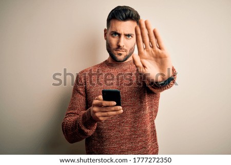 Young handsome man having conversation using smartphone over white background with open hand doing stop sign with serious and confident expression, defense gesture