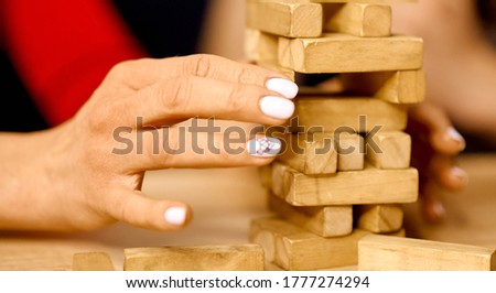 Woman pulls out one block of wooden game falling tower