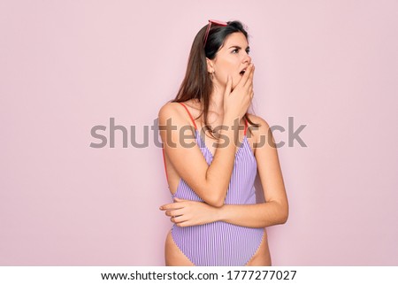 Young beautiful fashion girl wearing swimwear swimsuit and sunglasses over pink background bored yawning tired covering mouth with hand. Restless and sleepiness.