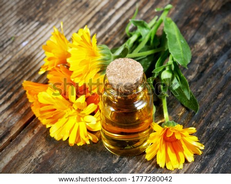 Bottle with marigold oil with marigold flowers on wooden background. Calendula flower.