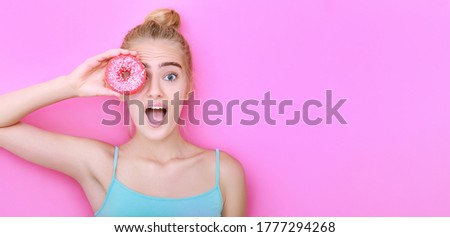 The girl covers her eyes with a donut and shows emotions of surprise. Pink isolated background