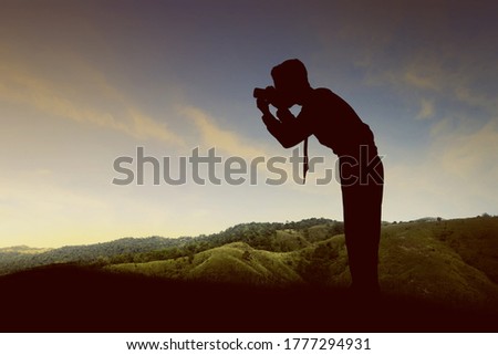 Silhouette of a businessman holding the camera on the top of the hills. World Photography Day
