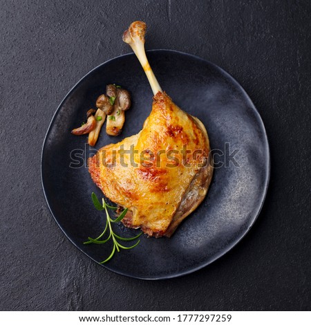 Duck leg confit with mushroom sauce on black plate. Slate background. Top view.