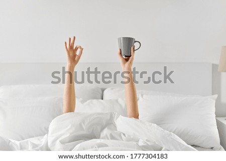 morning, comfort and people concept - young woman with cup of coffee lying in bed and showing ok hand sign at home bedroom Royalty-Free Stock Photo #1777304183