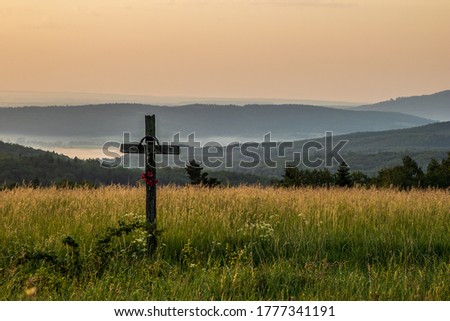 A roadside cross among a blooming meadow and hills