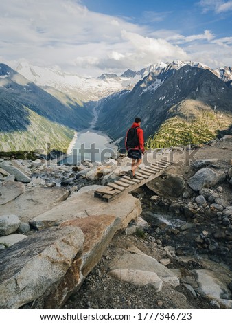 A man with a backpack walks along a mountain path. Walks along a rocky path against the sky and clouds. Traveling with a backpack.