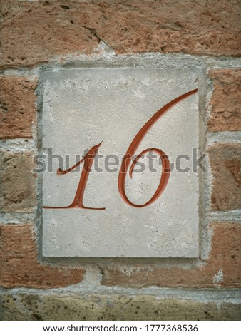 Engraved number 16, red house number on the wall sixteen