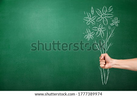 Human hand with drawn flowers on green chalkboard