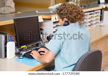 Rear view of female nurse answering telephone while working on computer at hospital reception Royalty-Free Stock Photo #177739580