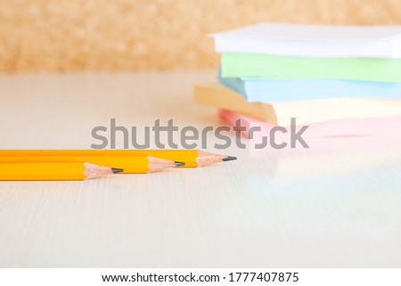 Yellow graphite pensils and blured stack of note paper on background at white office desk table. Close up view