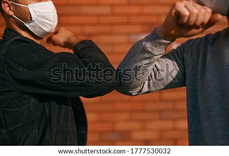 Crop men in masks greeting each other with elbow bump while keeping social distance during coronavirus epidemic on street Royalty-Free Stock Photo #1777530032