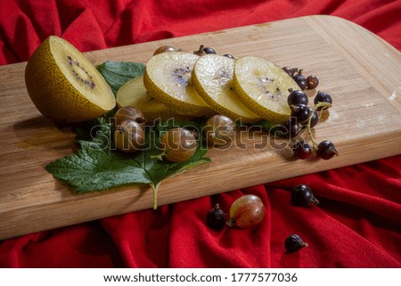 Kiwi sliced, gooseberries and black currants with leaves on a wooden board on a  red background