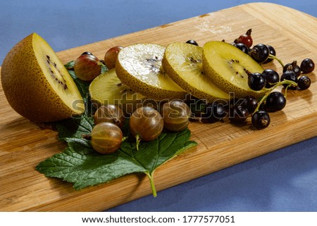 Kiwi sliced, gooseberries and black currants with leaves on a wooden board on a blue  background