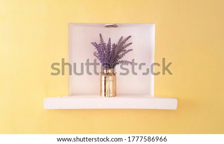 Golden pot with lavander flowers encased in a white square on a yellow wall - interesting architectural detail in interior design