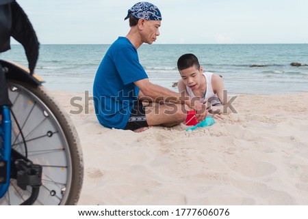 Asian special child playing sand and crawls happily on the beach near the wheelchair with his father,Sea nature background,Natural therapy,Life in the education age, Happy disabled kid travel concept.