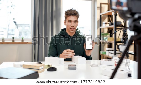 Young male technology blogger recording video blog or vlog about new smartphone and other gadgets at home studio. Blogging, Work from Home concept. Focus on face. Web Banner Royalty-Free Stock Photo #1777619882