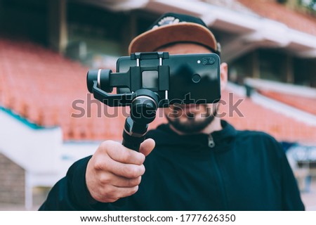 Blogger in the stadium shoots video on a smartphone with a manual camera stabilizer Royalty-Free Stock Photo #1777626350