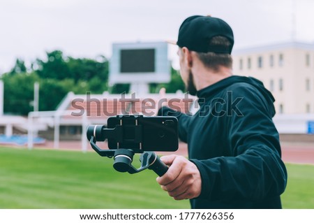 Blogger in the stadium shoots video on a smartphone with a manual camera stabilizer Royalty-Free Stock Photo #1777626356