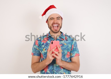 Young caucasian man wearing hawaiian shirt and Christmas hat over isolated white background ,taking a selfie  celebrating success