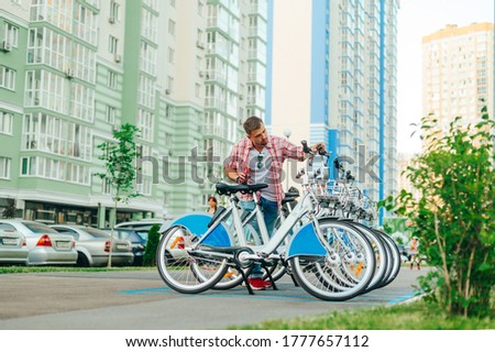 Male tourist chooses a bicycle in the parking lot of Schering. A man rents a bicycle from a row on a background of colored buildings. Bicycle rental for walking