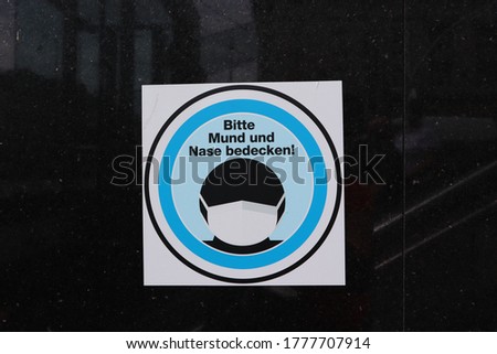 A blue, black and white sticker on a darkened window on an underground train in Vienna, Austria which shows a masked silhouette and says in German: please cover mouth and nose.