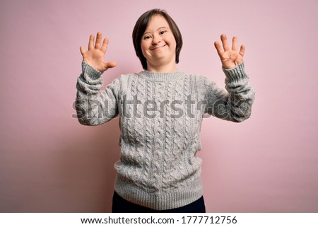 Young down syndrome woman wearing casual sweater over isolated background showing and pointing up with fingers number nine while smiling confident and happy.