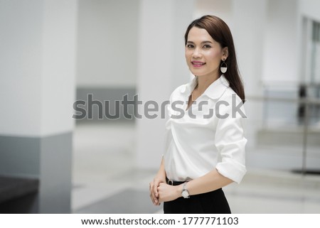 Portrait of a cheerful middle-age businesswoman in business suit stands in the company building with confidence arms crossed. Modern business woman in the office with copy space. Business stock photo.