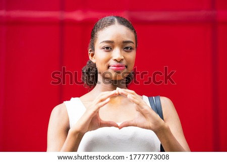 Young business woman giving an "OK" hand sign in front of a red wall