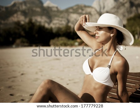 Young woman in white swimsuit sunbathes sitting on sunbed.