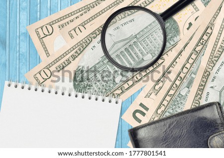 10 US dollars bills and magnifying glass with black purse and notepad. Concept of counterfeit money. Search for differences in details on money bills to detect fake