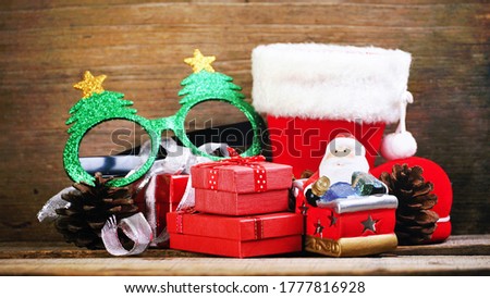 Red gift boxes with pinecones and green fancy glitter eyeglasses and santa claus model and wood christmas tree decorate on wood table.    