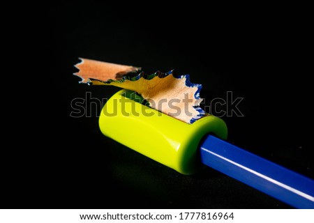 A green sharpener sharpening a blue pencil. Macro pictures within the image are sharpeners, pencils, sawdust, on a black background.