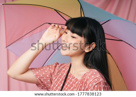 Beautiful asian thai long dark hair woman in pink dress holding rainbow umbrella over pink background. Fashion portrait.