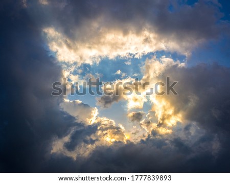 Dramatic sunset sky background. Beautiful sky with bright golden sunlight rays through the dark storm clouds.