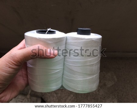 The big white rope in the hand, used for sewing sacks in industrial applications.