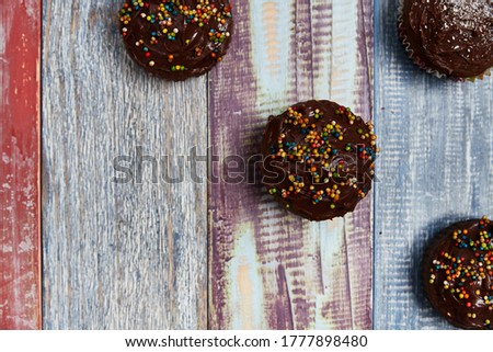 several chocolate cupcakes with decorations on the top and right side of the image on a background of coloured boards for a baby shower, photo taken from above, party concept, background, colours