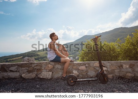 Young man riding an electric scooter on mountain range. Rest after a long trip, enjoying fresh air and beautiful scenic views. Ecological transportation concept
